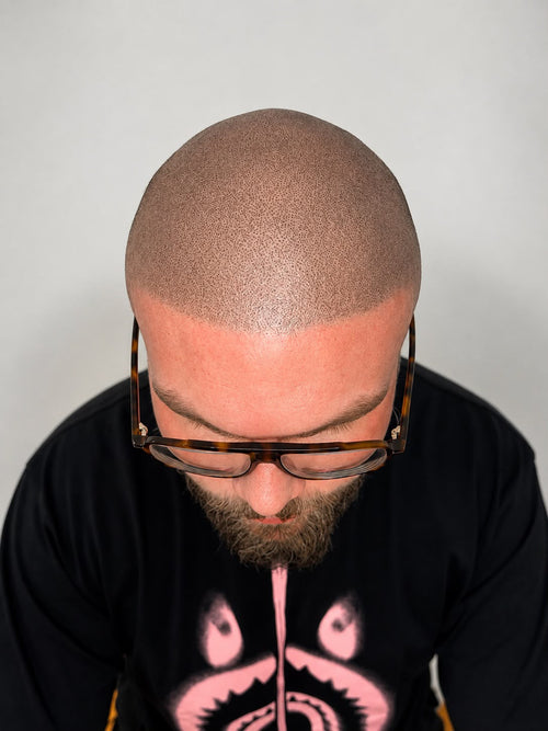 Man wearing glasses and a black shirt with pink design against a plain background