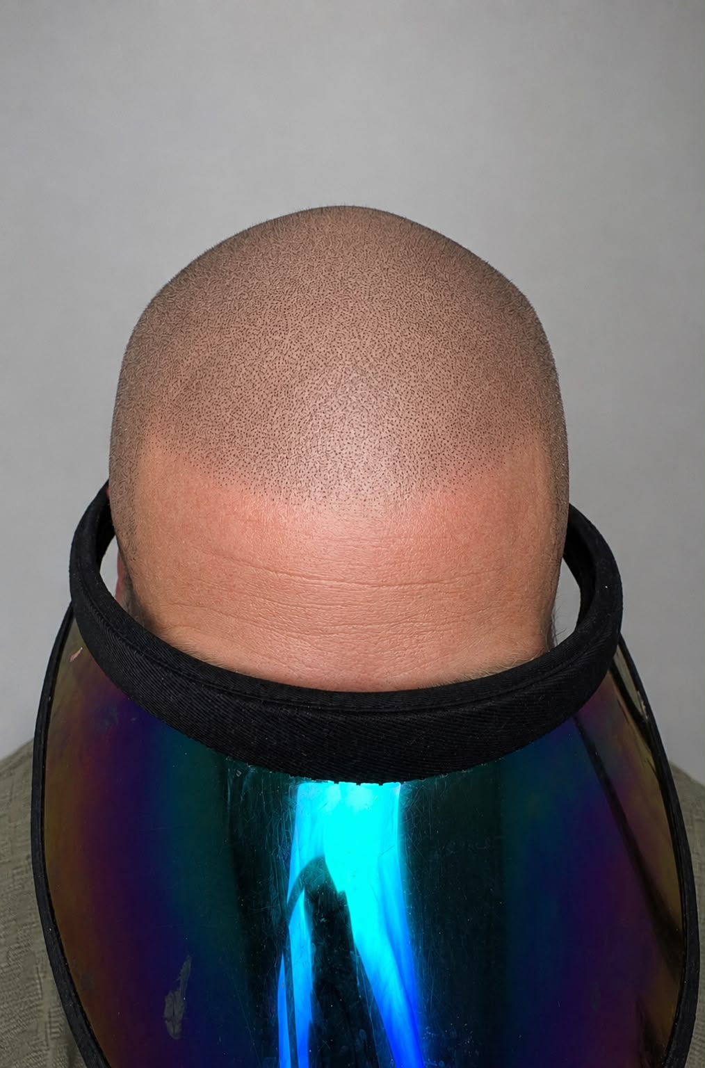 Close-up of a bald head with a colorful visor worn by a person.